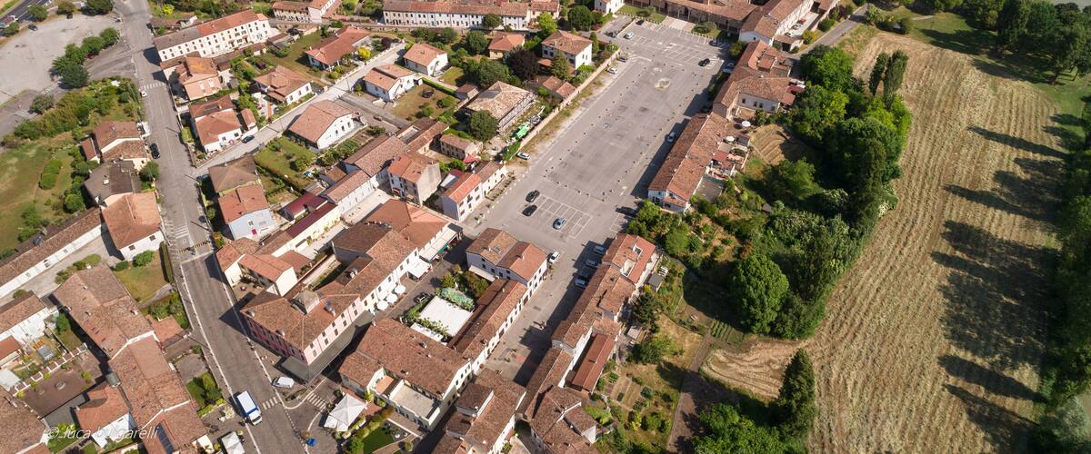 An aerial view of a town with a central square, surrounding buildings, and adjacent agricultural fields.