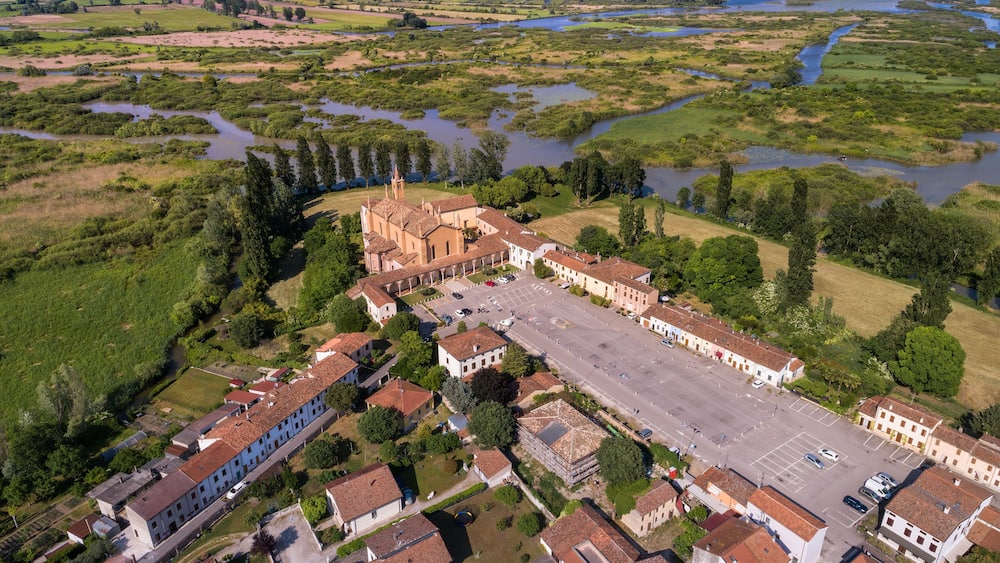 An aerial view of a historic town with a prominent church, surrounded by lush greenery and a river.