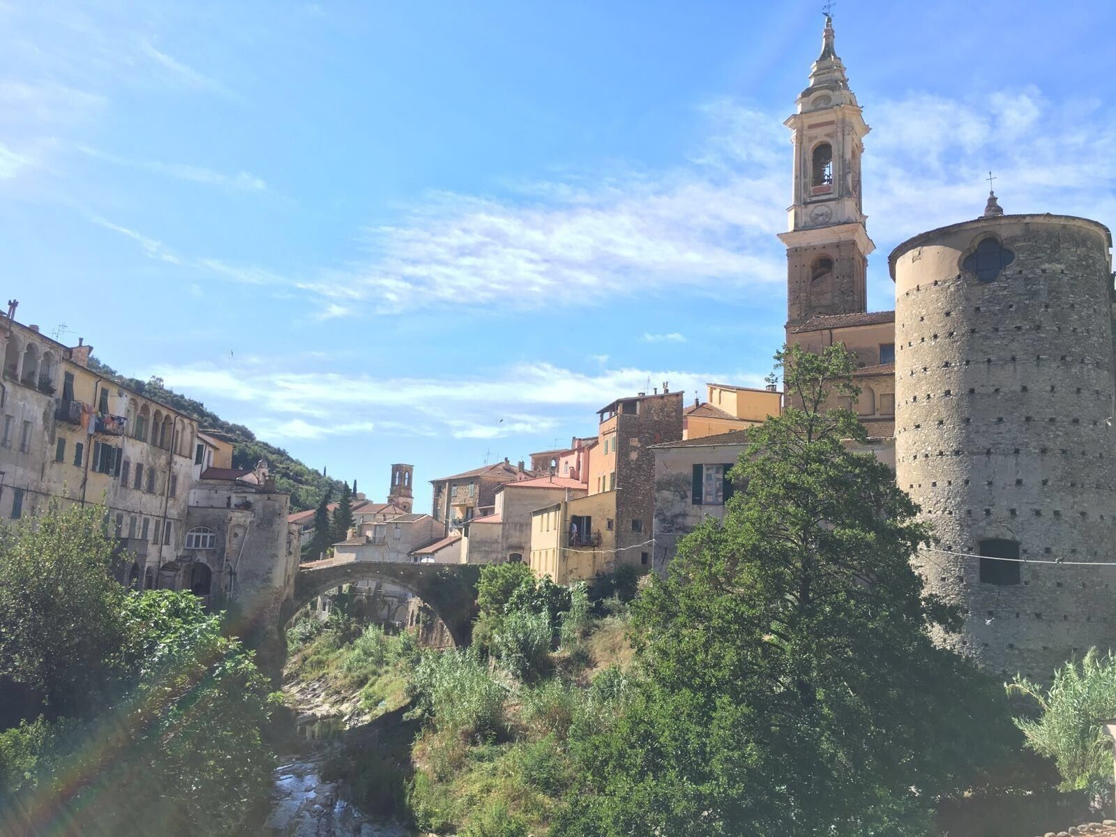 A historic town with a prominent tower, a round tower, and a stone bridge over a river.