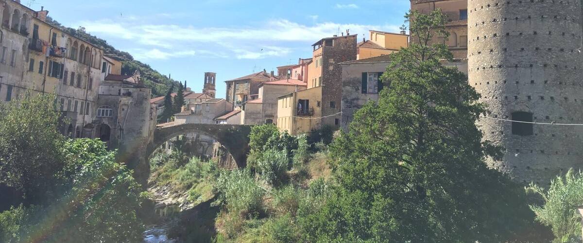 A historic town with a prominent tower, a round tower, and a stone bridge over a river.