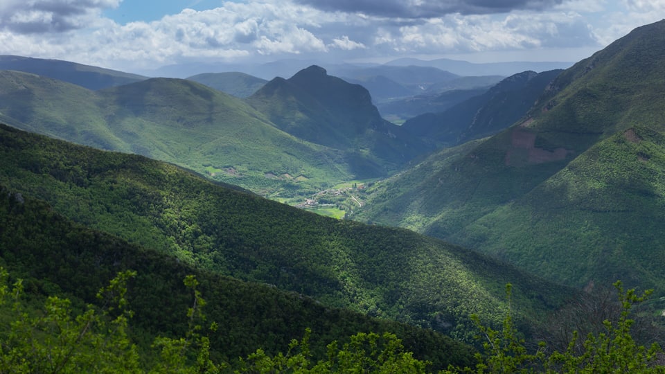 A valley with lush green hills and a small village nestled in the valley.