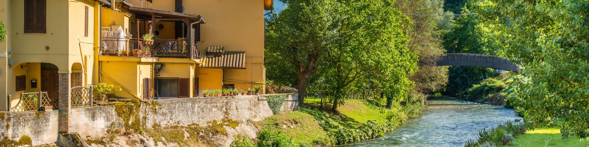 Un río serpentea por un exuberante valle con un puente, rodeado de vegetación y un edificio amarillo con balcón.