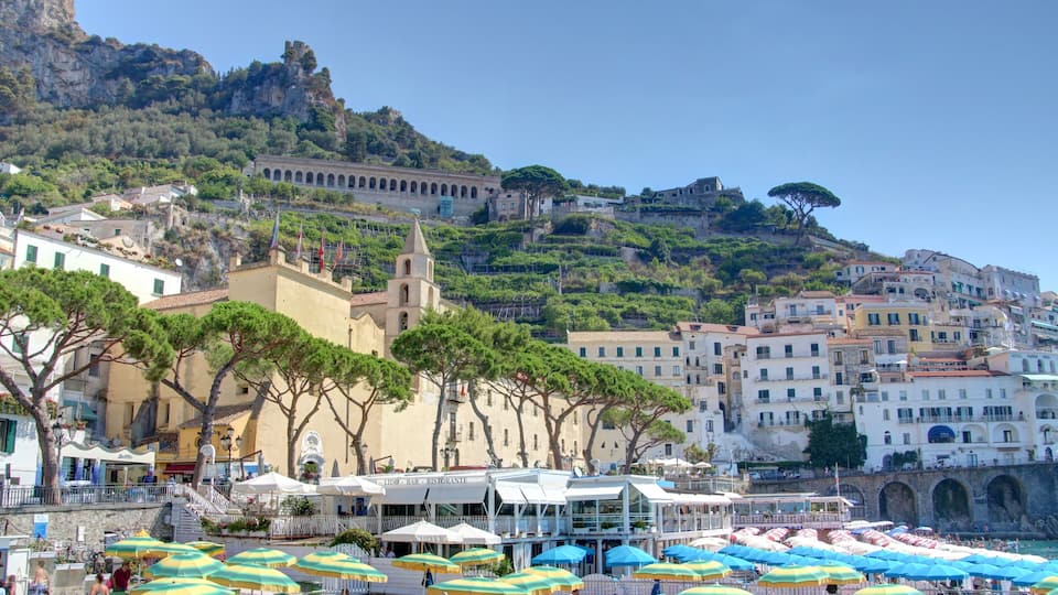 A coastal town with a prominent church, a hill with a castle, and a beach with umbrellas.