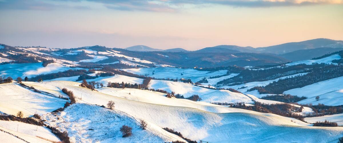 A snow-covered landscape with rolling hills and distant mountains under a clear sky.