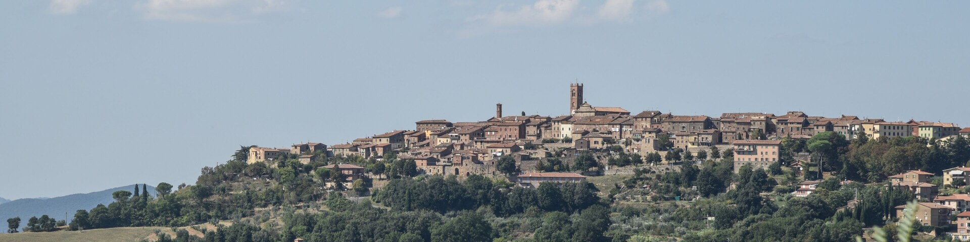 Un pueblo en la ladera de una colina con edificios históricos, una torre destacada y abundante vegetación.
