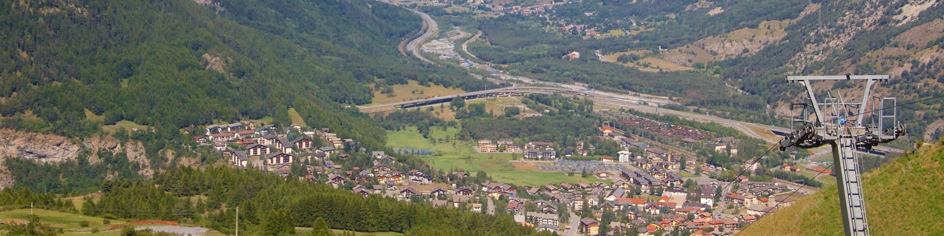 A mountainous landscape with a valley, a winding road, and a ski lift.