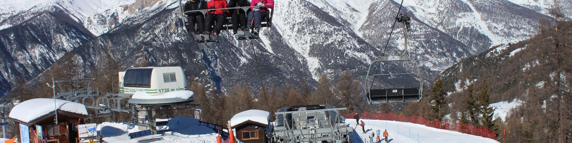 A ski lift with skiers and a mountain backdrop.