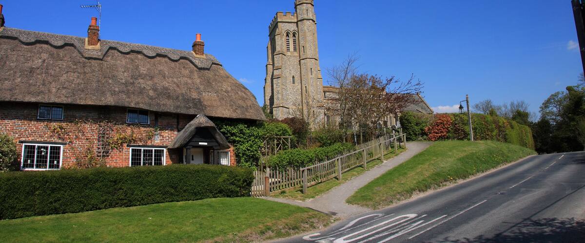 A thatched-roof cottage with a brick exterior, a tall stone tower, and a clear blue sky.