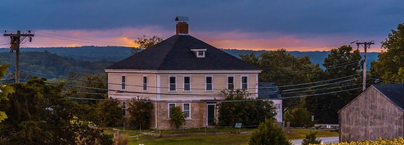 Uma casa rodeada por um campo de girassóis sob um céu nublado.