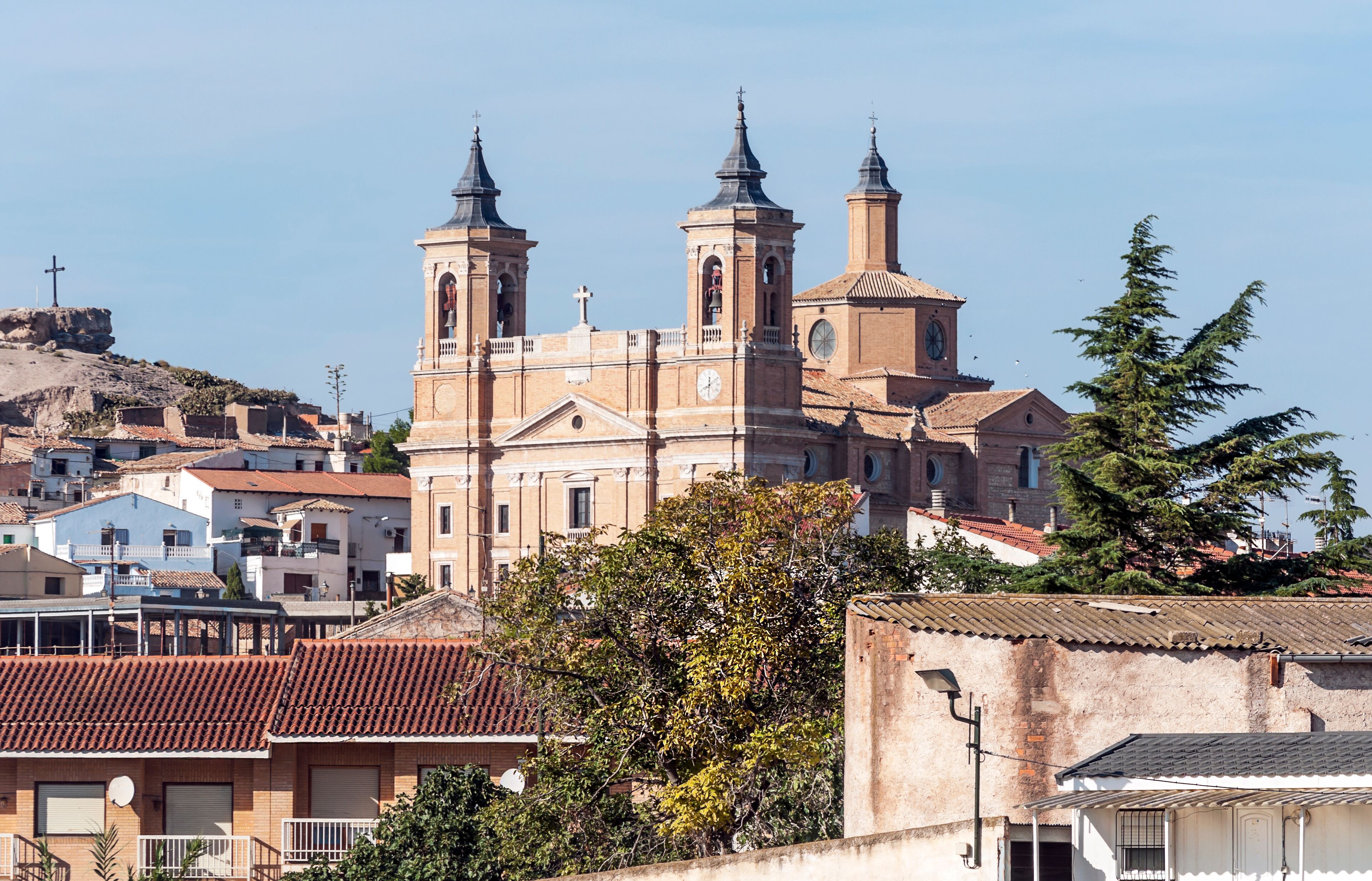 A historic church with two bell towers, surrounded by residential buildings and a hill in the background.