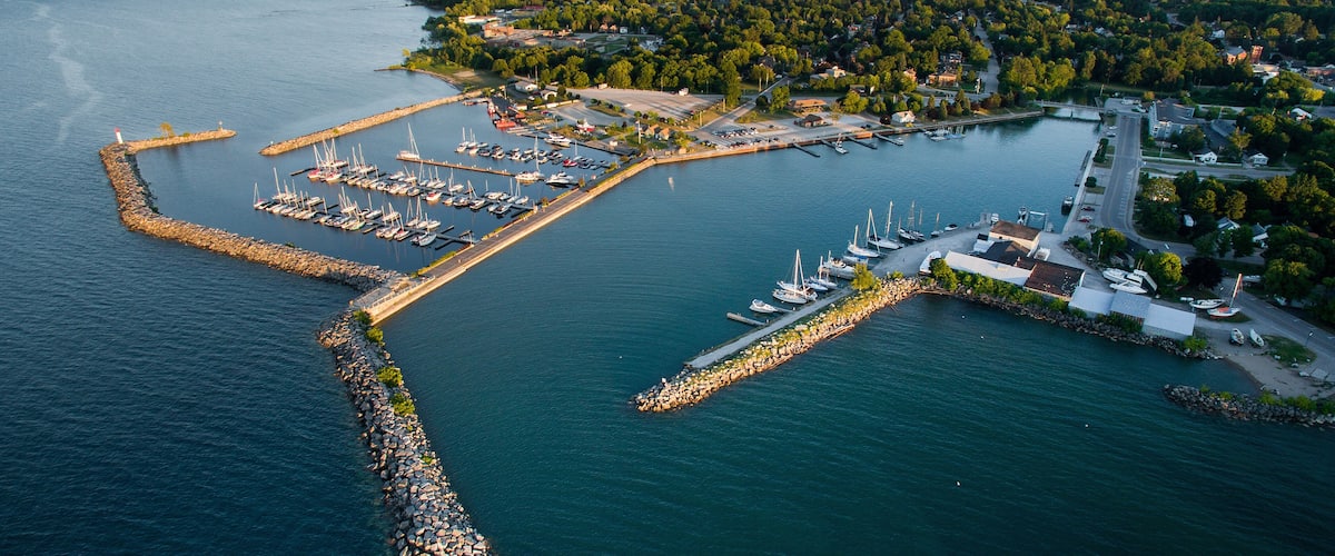 An aerial view of a marina with boats, a lighthouse, and a forested area.