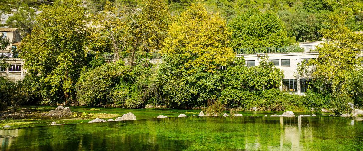 A serene lake surrounded by lush greenery and a modern building with a balcony overlooking the water.