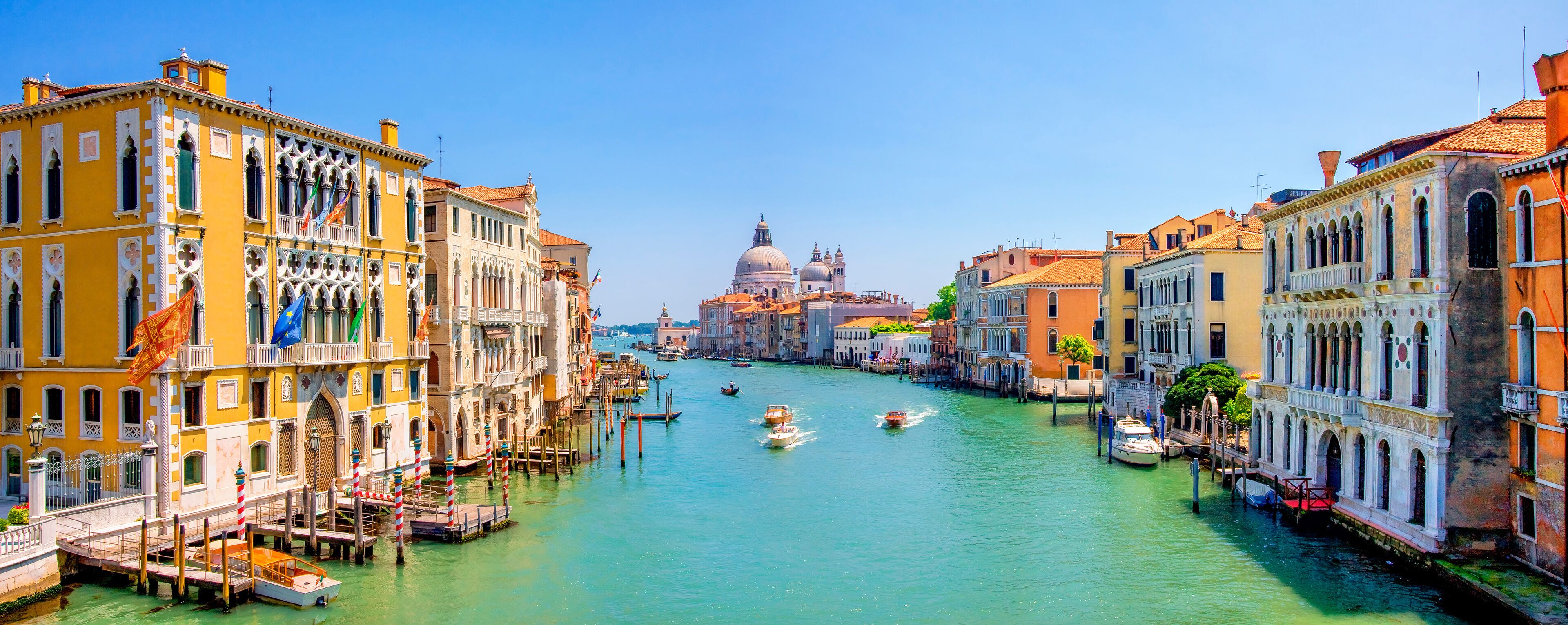 A canal with boats, historic buildings, and a prominent dome in Venice.