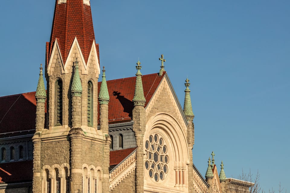 A church with a tall spire, arched windows, and a large circular stained glass window.