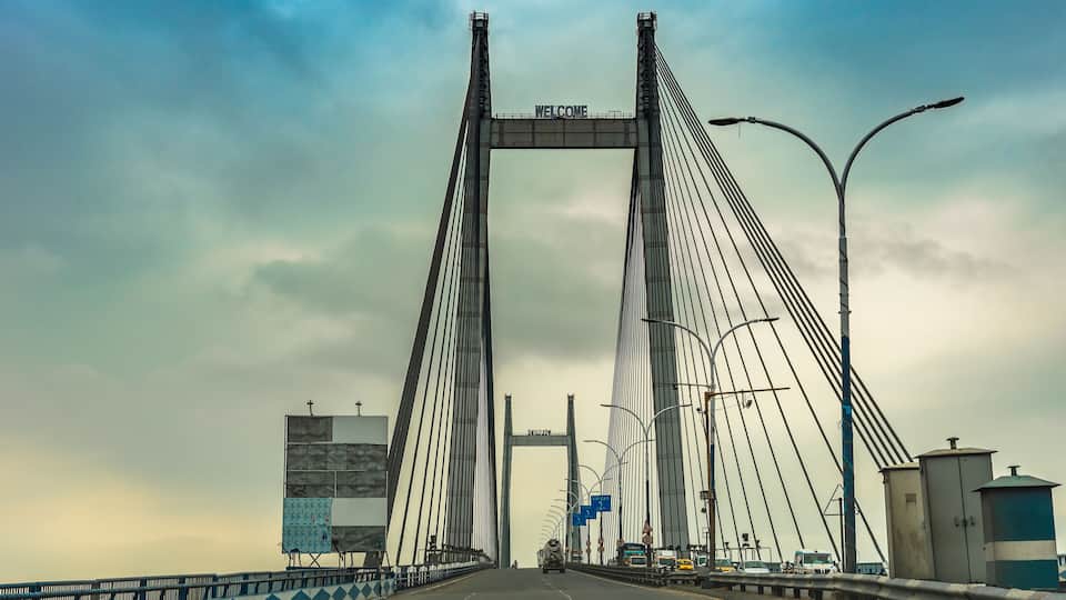 A large suspension bridge with a 'WELCOME' sign, featuring a road with vehicles and street lamps.