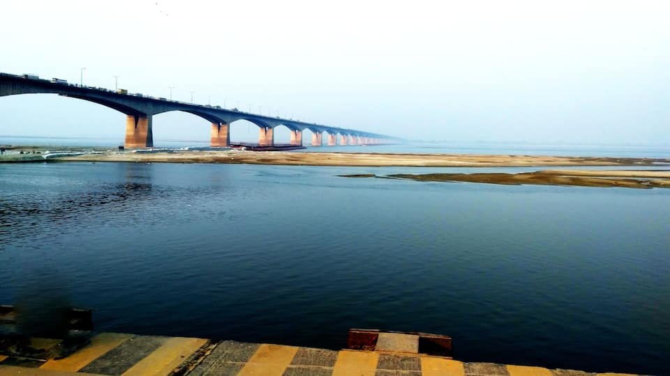 A long bridge spanning a wide river with a sandy bank on one side and a concrete walkway on the other.