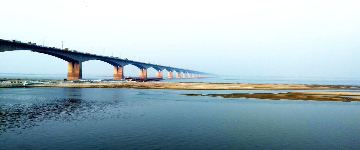 A long bridge spanning a wide river with a sandy bank on one side and a concrete walkway on the other.