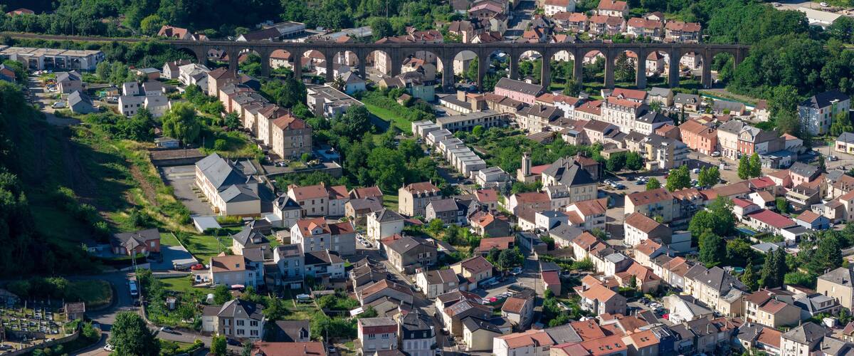 An aerial view of a town with a prominent viaduct, residential buildings, and surrounding greenery.