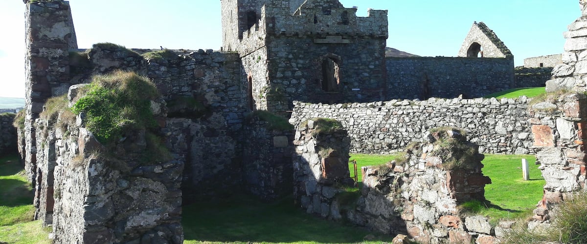 A medieval stone castle with ruins, including a tower and walls, set in a grassy area.