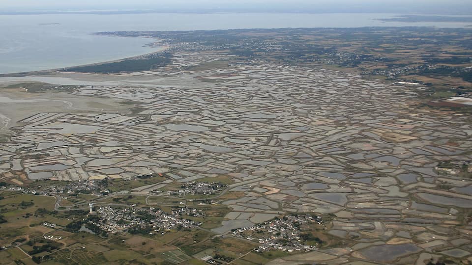 An aerial view of a coastal region with extensive salt pans and a small town.