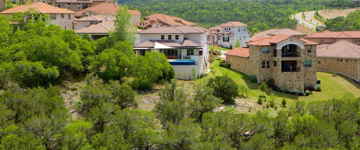 A hillside village with terracotta-roofed houses, lush greenery, and a winding road.