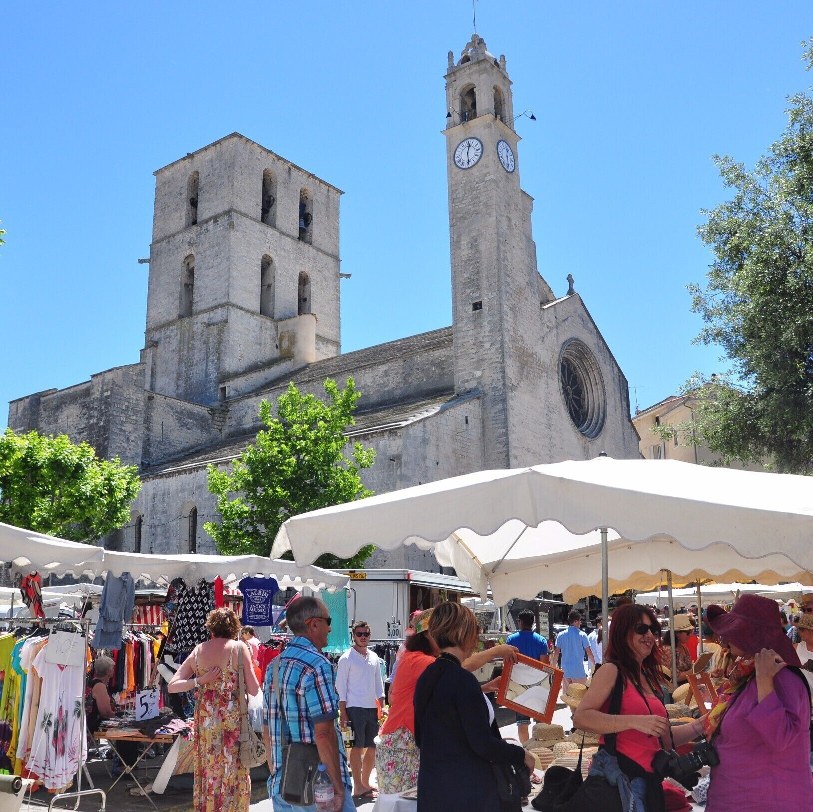 A market with people and stalls, a clock tower, and a church in the background.