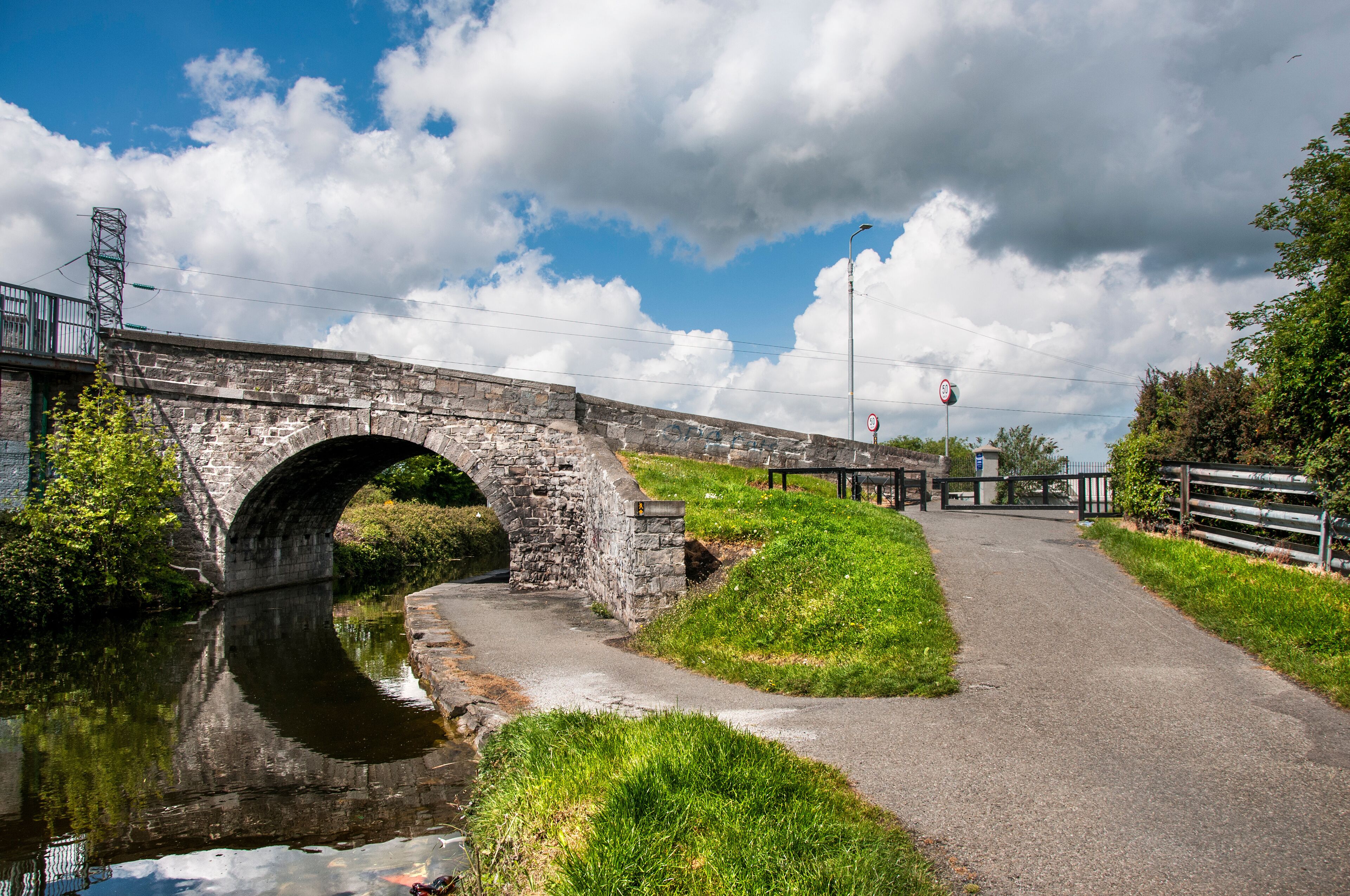 A stone bridge over a canal with a grassy path beside it.