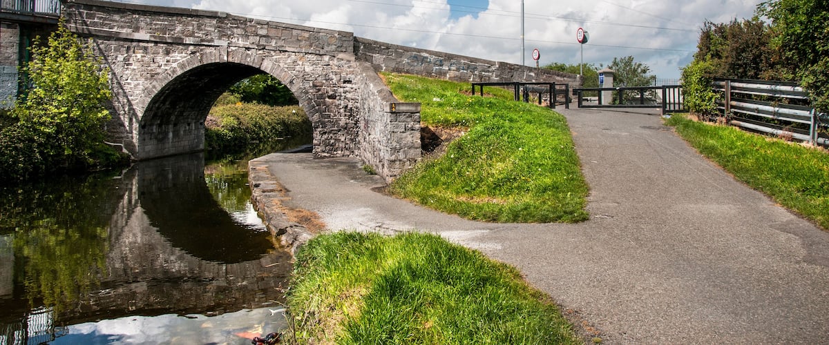 A stone bridge over a canal with a grassy path beside it.