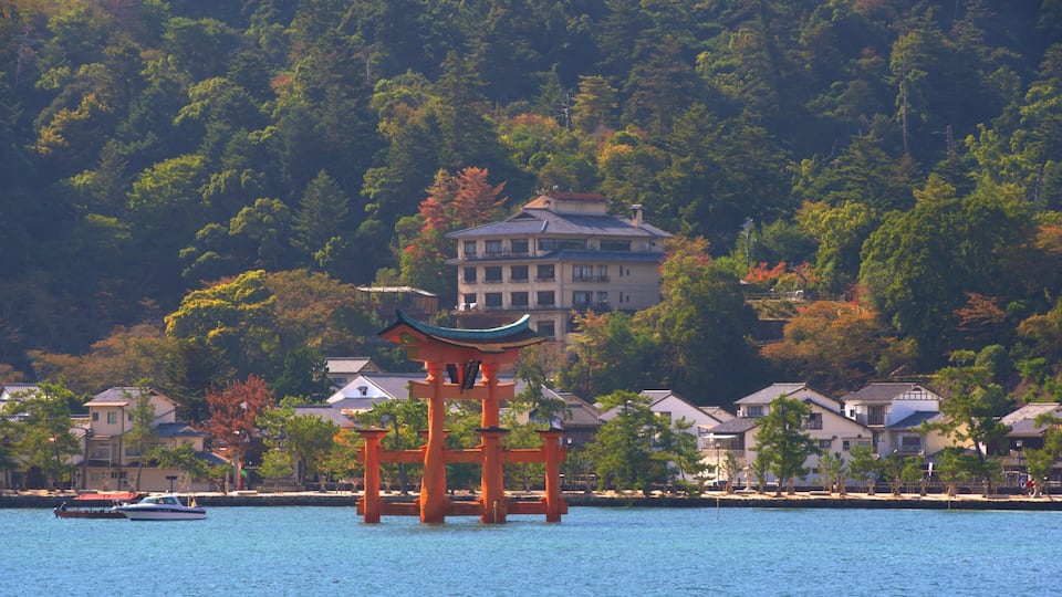 A traditional Japanese torii gate in the foreground with a body of water and houses in the background.