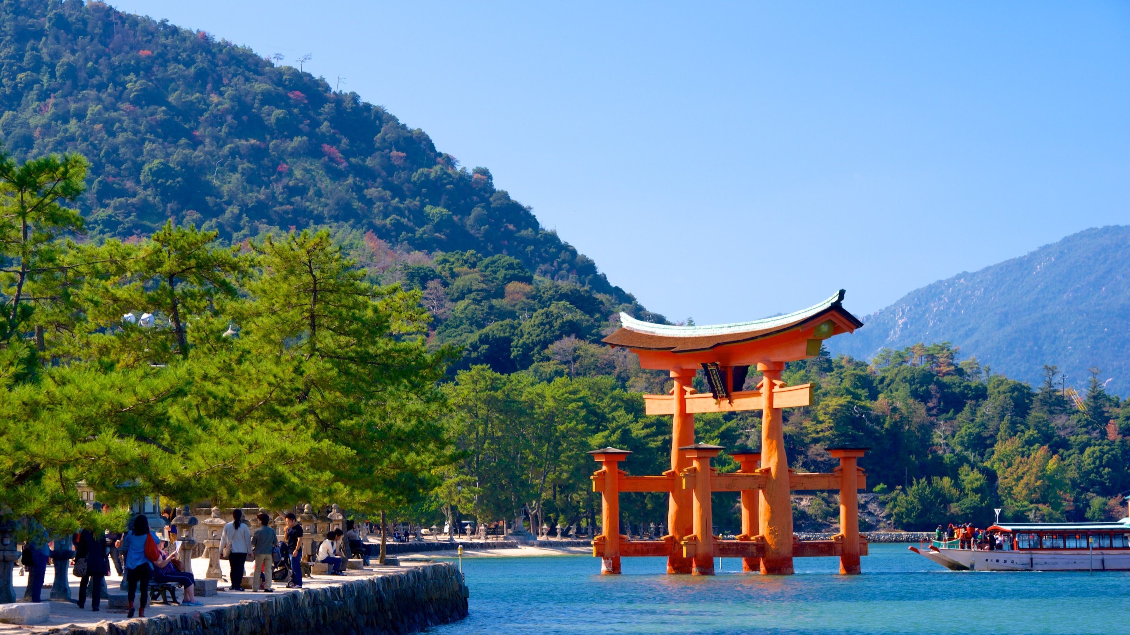 A traditional Japanese torii gate in a serene lakeside setting with lush greenery and mountains in the background.