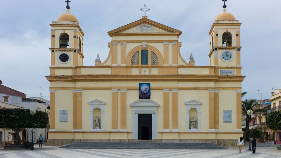 A yellow church with two bell towers and a central dome, featuring a clock and a portrait.