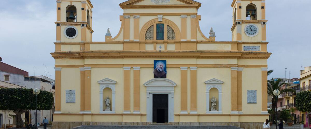 A yellow church with two bell towers and a central dome, featuring a clock and a portrait.