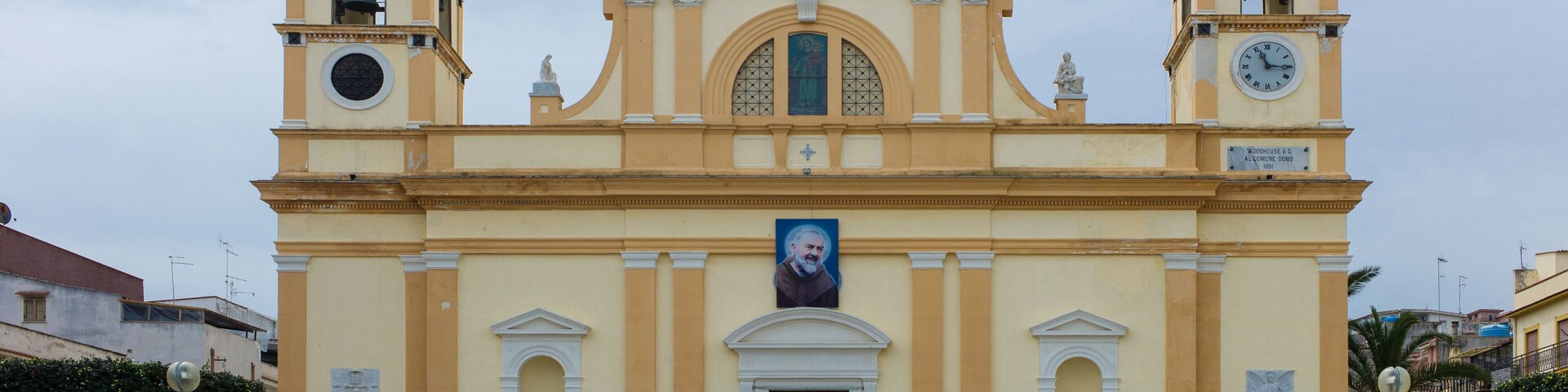 A yellow church with two bell towers and a central dome, featuring a clock and a portrait.