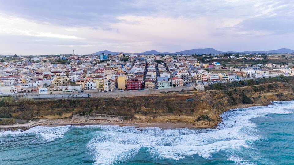 A coastal cityscape with buildings, a cliff, and the ocean.