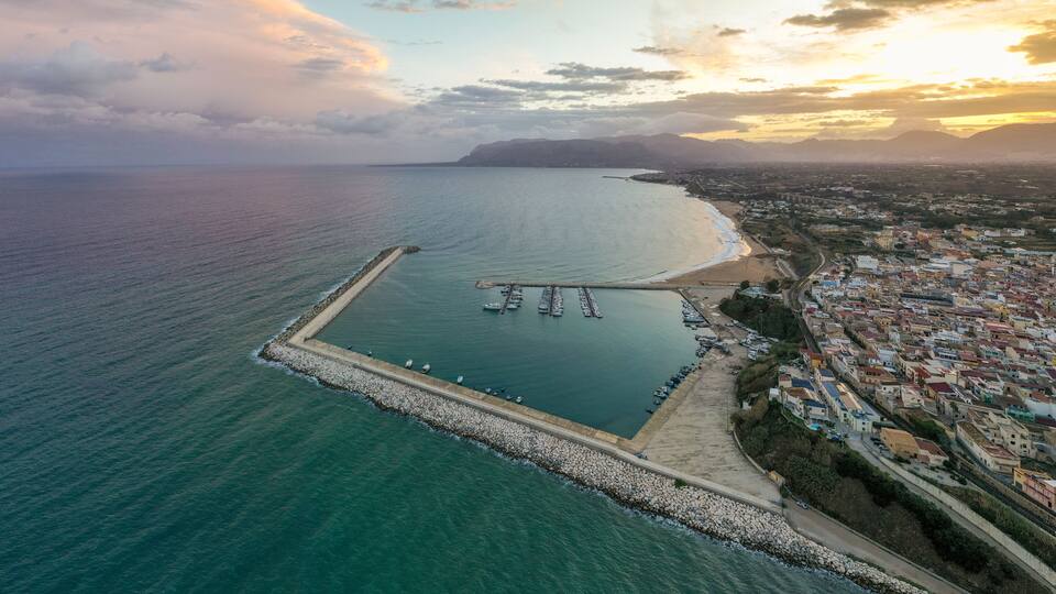A coastal town with a marina, a breakwater, and a mountain range in the distance.