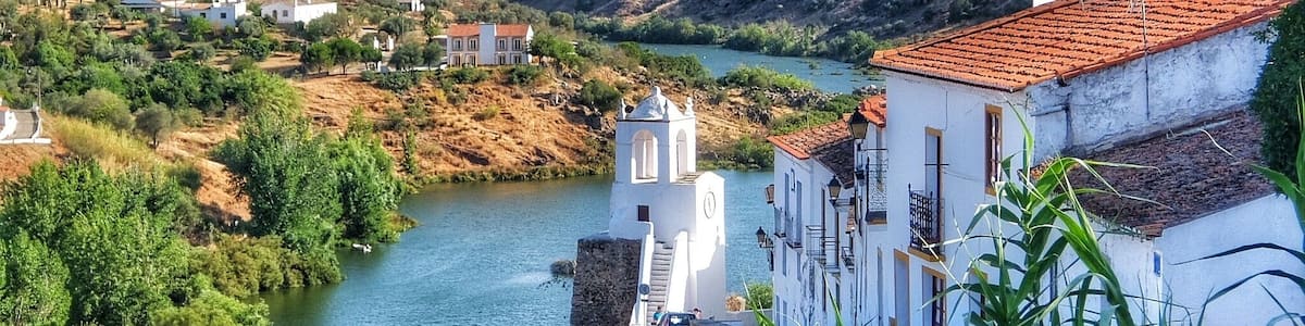 A river flowing through a valley with white buildings and a church with a bell tower.