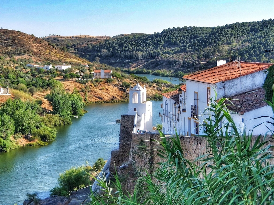 Un río serpentea por un valle con edificios blancos y una iglesia con campanario.