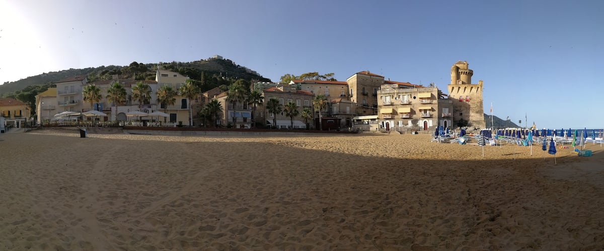 A beach with buildings, palm trees, and a tower.