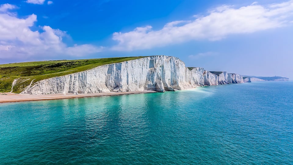 A coastal landscape with white cliffs, a sandy beach, and turquoise waters.