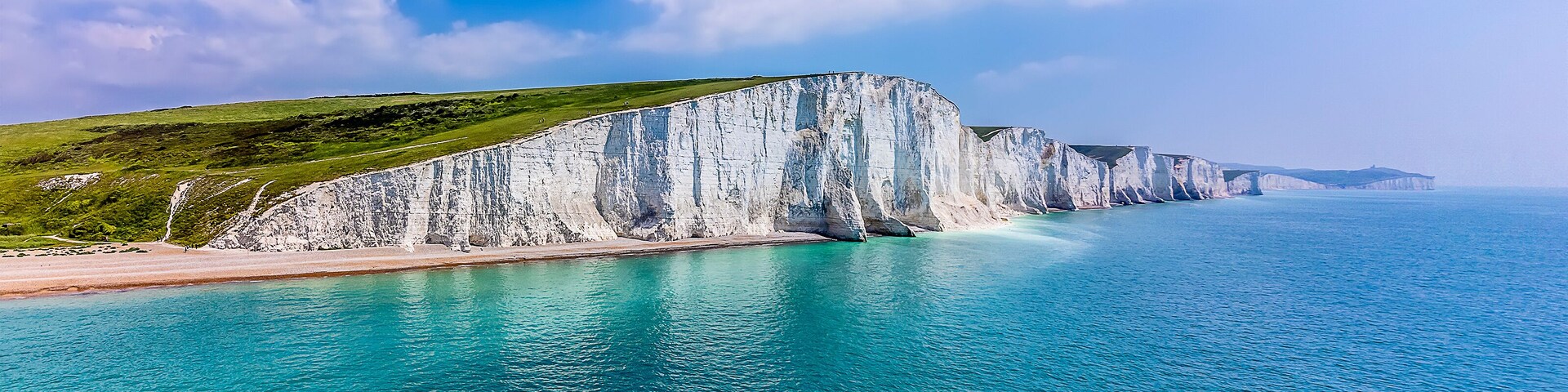 Un paisaje costero con acantilados blancos, una playa de arena y aguas turquesas.