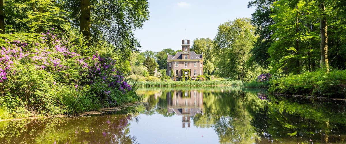 A historic house surrounded by lush greenery and a calm river.