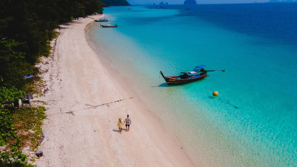 A beach with clear turquoise water, a boat, and a distant island.