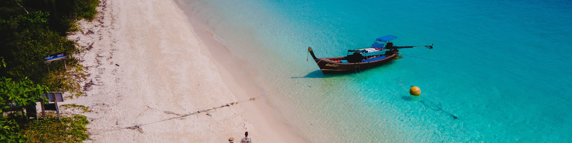 A beach with clear turquoise water, a boat, and a distant island.