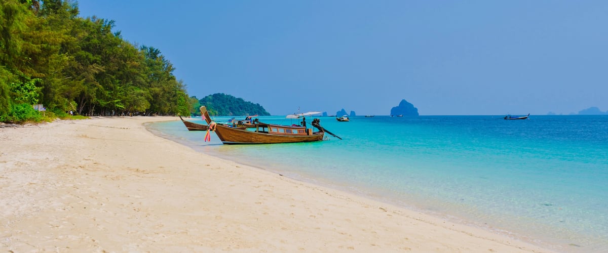 A beach with clear turquoise water, a sandy shore, and several traditional boats.