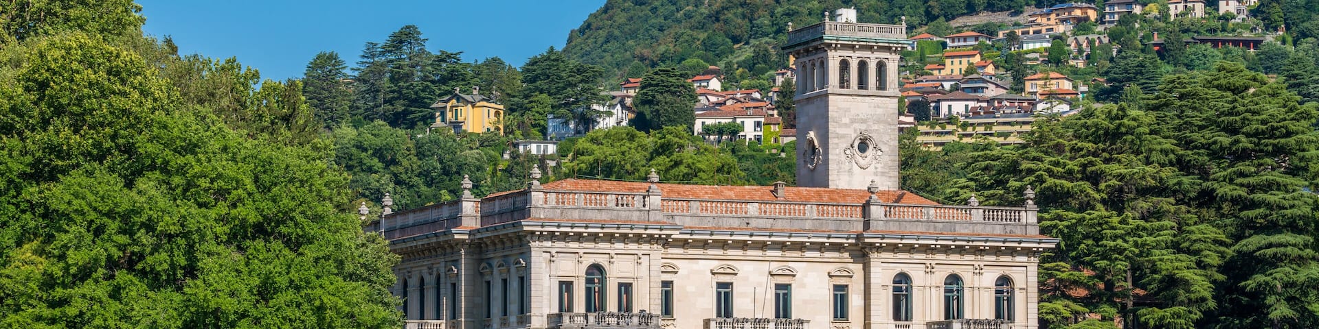 A historic building with a clock tower, surrounded by lush greenery and a body of water.