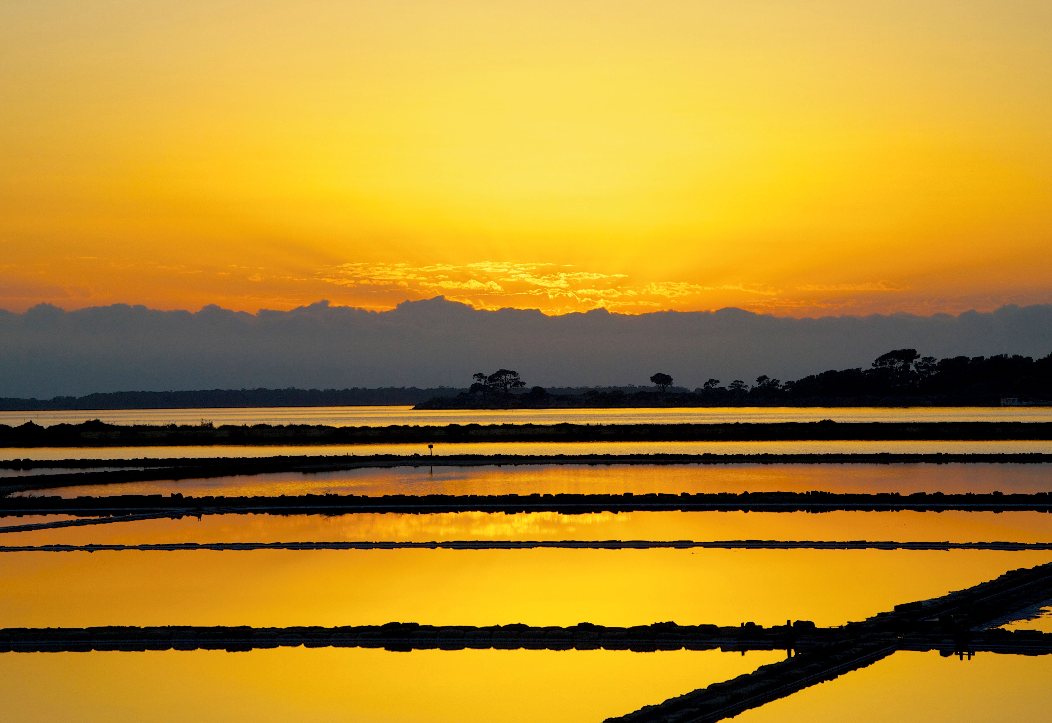 A sunset over a series of water-filled rice paddies.