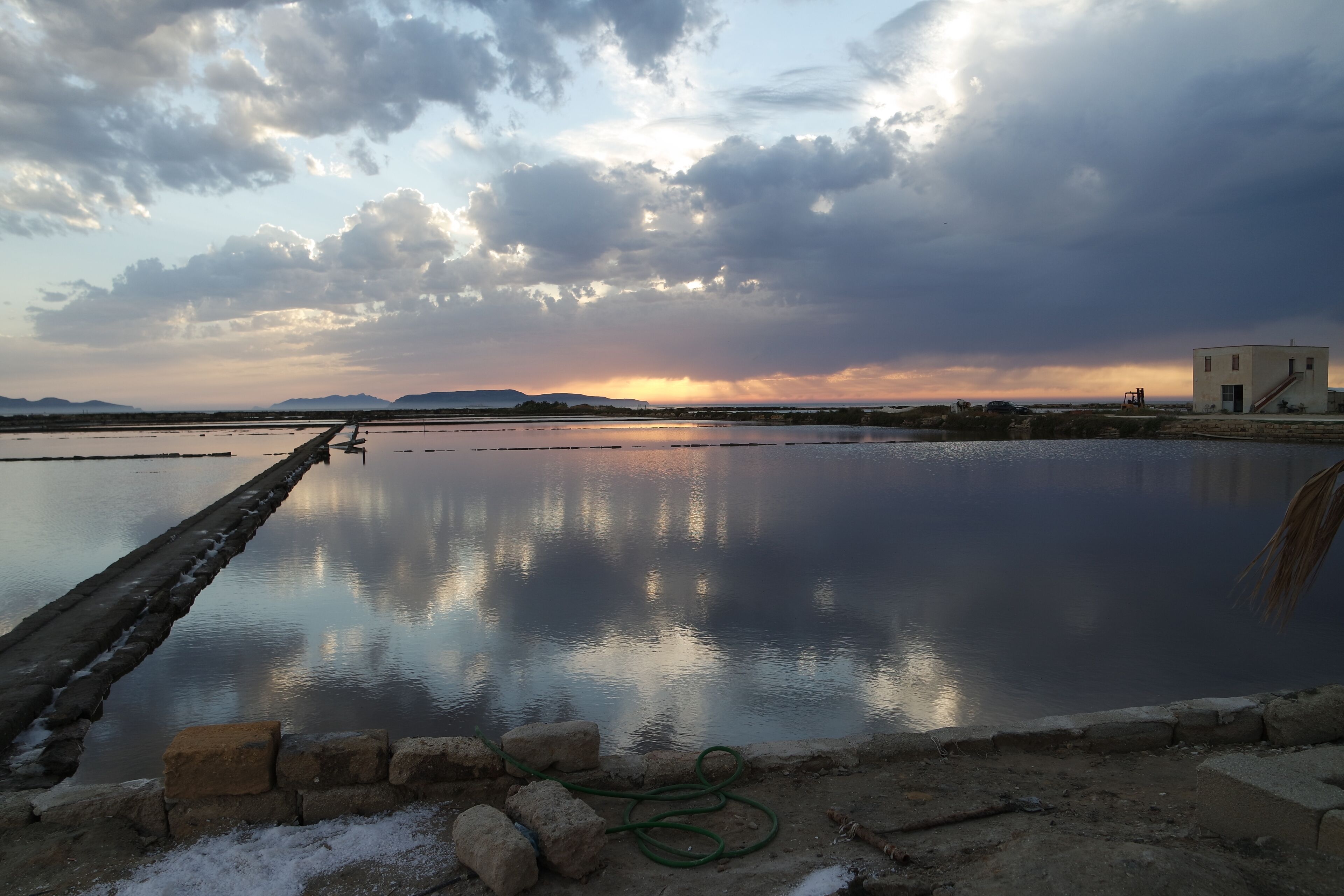 A calm lake with a dock, a small building, and distant mountains under a cloudy sky.