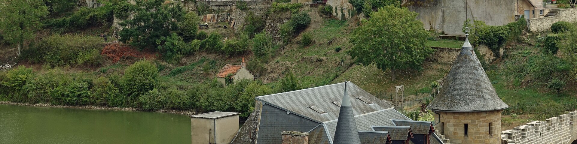 Um castelo histórico e edifícios medievais numa colina com vista para um rio.