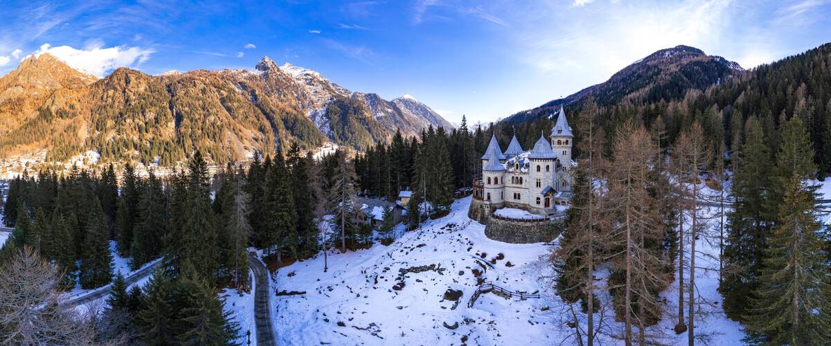 A snow-covered mountain landscape with a historic castle surrounded by dense forests.
