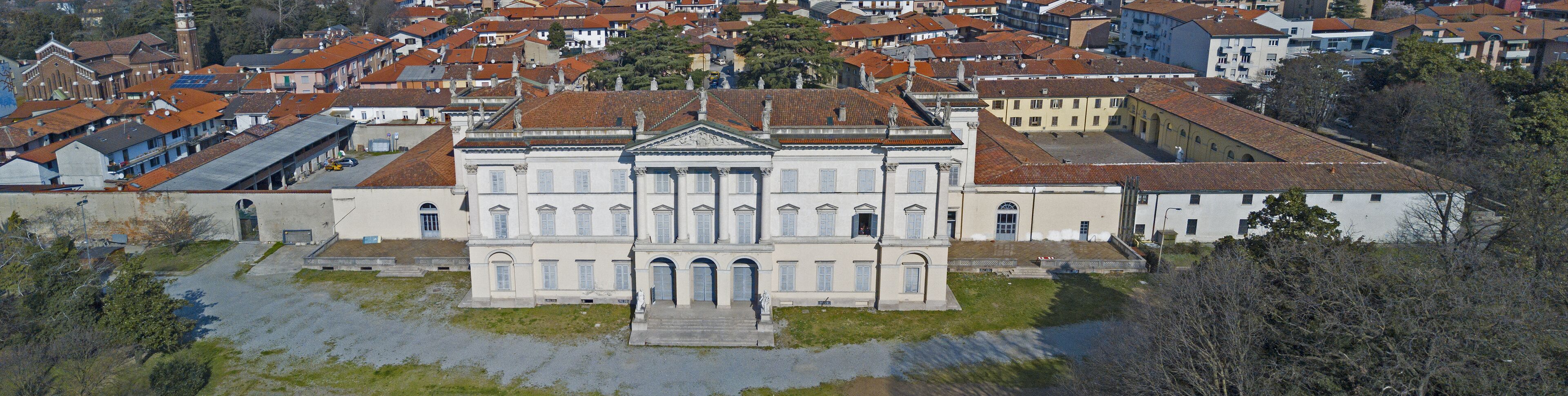 A large white building with a central entrance and statues on the roof, surrounded by red-roofed houses.